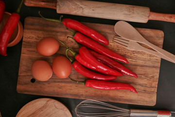 A few cayenne paper, eggs, and cooking utensils on a wooden background.