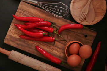 A few cayenne paper, eggs, and cooking utensils on a wooden background.