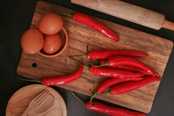 A few cayenne paper (Capsicum annuum), eggs, and cooking utensils on a wooden background.