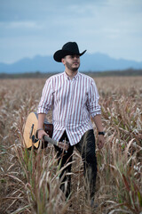 JOVEN MEXICANO CANTANDO CON SU GUITARRA USA SOMBRERO Y TIENE BARBA