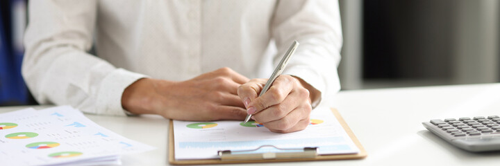 Businesswoman holds pen and makes adjustments in report of financial indicators in charts