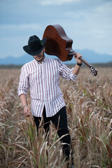 JOVEN MEXICANO CANTANDO CON SU GUITARRA USA SOMBRERO Y TIENE BARBA