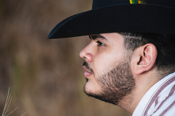 JOVEN MEXICANO CANTANDO CON SU GUITARRA USA SOMBRERO Y TIENE BARBA
