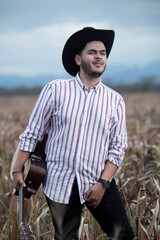 JOVEN MEXICANO CANTANDO CON SU GUITARRA USA SOMBRERO Y TIENE BARBA