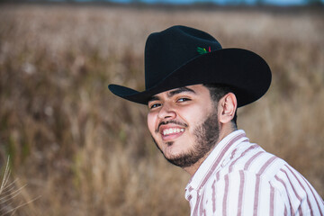 JOVEN MEXICANO CANTANDO CON SU GUITARRA USA SOMBRERO Y TIENE BARBA