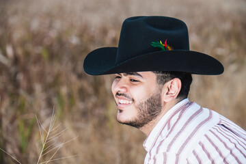 JOVEN MEXICANO CANTANDO CON SU GUITARRA USA SOMBRERO Y TIENE BARBA