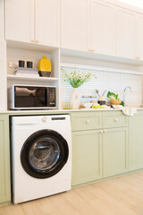 Modern green kitchen interior with washing machine and microwave.