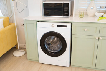 Modern green kitchen interior with washing machine and microwave.