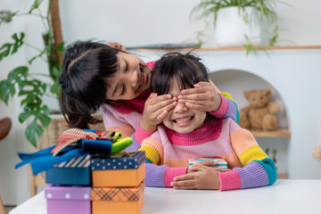 Obraz premium Little girl making present to little happy kid girl holding gift box, closing eyes of cute smiling excited with birthday surprise from her sister
