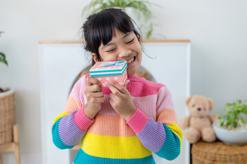 Little Asian girl smile and excited and holding red gift box in living room background. child holding gift box in Christmas and New year.Asian child girl smile and surprise.