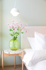 Green glass vase with bouquet of beautiful puppy flowers with lamp on side table in bedroom.