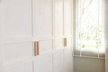 Fototapeta na wymiar Minimal white closet or wardrobe with wood door handles. Close-up and selective focus at the knob handle.