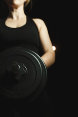 Young girl exercising with a heavy dumbbell in a dark room.