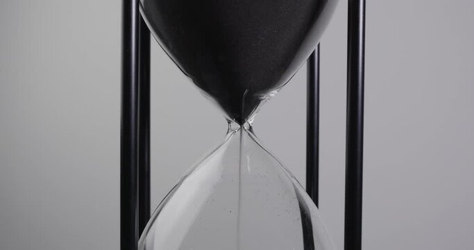 Closeup of sand timer clock with sand flowing from through hourglass on white background.
