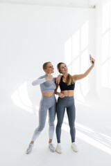 Fototapeta premium Two sports women meet at gym, making selfie photo while standing together at gym
