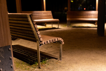 Fototapeta na wymiar A park shed with empty benches during a pandemic. Meeting places without people. The photo was taken at night with artificial street lighting.