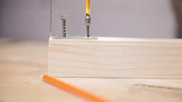 A cross-head screwdriver screws a self-tapping screw into a wooden bar for attaching a metal corner, close-up