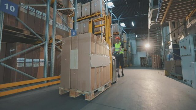Worker with forklift in the warehouse. The worker walks through the warehouse. A worker in a warehouse carries a electric hydraulic forklift