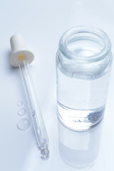 glass transparent jar and a cosmetic pipette with liquid droplets on a white background.