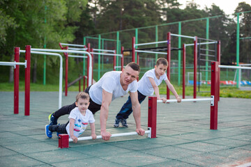 Caucasian man goes in for sports on the sports ground with his sons.