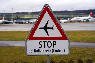 Triangle warning sign at Zürich Airport with text stop in case of taxiing airplanes on a rainy winter day. Photo taken December 26th, 2021, Zurich, Switzerland.