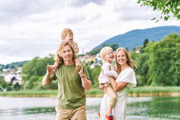 Fototapeta na wymiar Outdoor portrait of beautiful family, young couple with preschooler boy and toddler girl posing next to lake or river