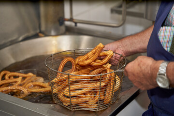 Unrecognizable senior cook removing churros from the boiling oil and placing them in a metal basket. Typical Spanish breakfast. 