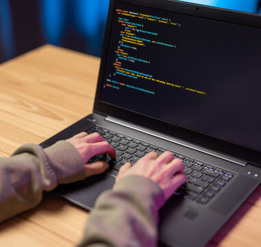 Close up of female developer typing on wireless laptop while writing web programm at home. Woman sitting at desk with portable computer.