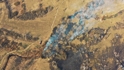 Aerial View. Spring Dry Grass Burns During Drought Hot Weather. Bush Fire And Smoke. Fire Engine, Fire Truck On Firefighting Operation. Wild Open Fire Destroys Grass. Ecological Problem Air Pollution