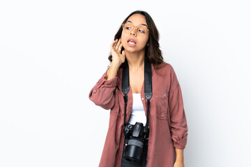 Young photographer woman over isolated white background listening to something by putting hand on the ear