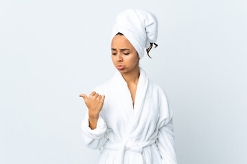 Young woman in bathrobe over isolated white background unhappy and pointing to the side