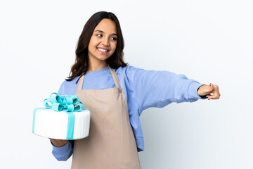 Pastry chef holding a big cake over isolated white background giving a thumbs up gesture