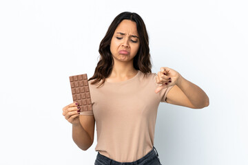 Young woman over isolated white background taking a chocolate tablet making bad signal