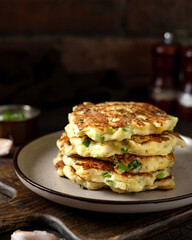 Homemade potato pancakes with cottage cheese and green onions in a ceramic plate on a dark background. A traditional dish of European cuisine from vegetables close-up	