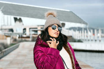 portrait of a woman with sunglasses and wool cap on a sunny autumn day walking in the city