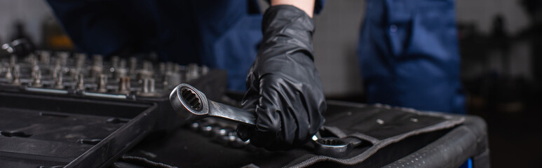 Cropped view of mechanic in glove holding wrench in garage, banner.