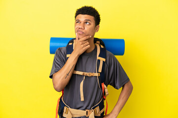 Young mountaineer African American man with a big backpack isolated on yellow background having doubts