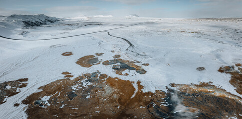 Aerial Drone panorama with hot steam coming from the ground. Hverir is geothermal area in Myvatn. Landscape covered with snow and orange ground.