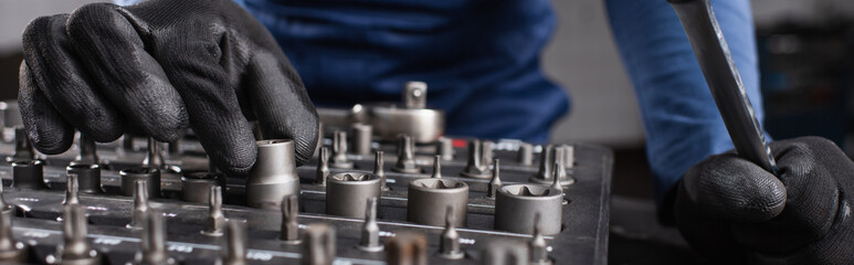 Naklejka premium Cropped view of mechanic in gloves taking tool in garage, banner.