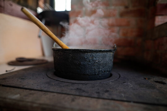 Cast iron cauldron boiling a goulash stew over a wood burning stove made from red bricks in the backyard of a rural house in Romania.