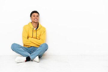 Young African American man sitting on the floor isolated on white background with arms crossed and looking forward