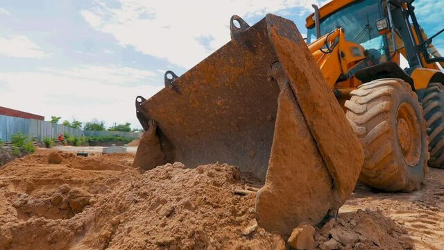 The tractor works at a construction site. Working process at a construction site. Tractor bucket close up