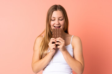 Teenager Ukrainian girl isolated on pink background eating a chocolate tablet
