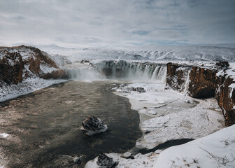 Drone shot of Godafoss waterfall, Iceland, taken from a high angle. Aerial view of the powerful cascade, river and snow covered rocks. Late autumn, early winter scene.
