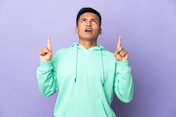 Young Ecuadorian man isolated on purple background surprised and pointing up