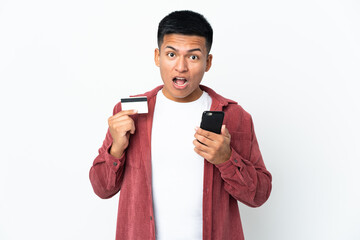 Young Ecuadorian man isolated on white background buying with the mobile and holding a credit card...