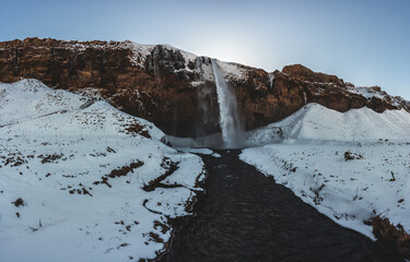 Seljalandsfoss waterfall in Iceland during winter with blue sky and snow and frozen landscape.