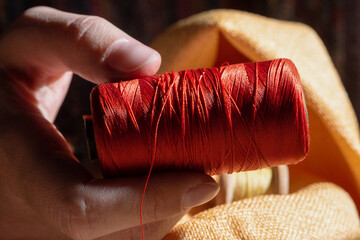 Sewing red thread spool in tailor hand close up.