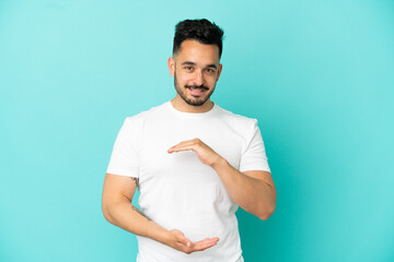 Young caucasian man isolated on blue background holding copyspace imaginary on the palm to insert...