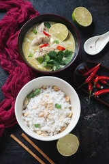 Green chicken curry and white rice with peanuts served in two bowls over dark brown stone background, vertical shot